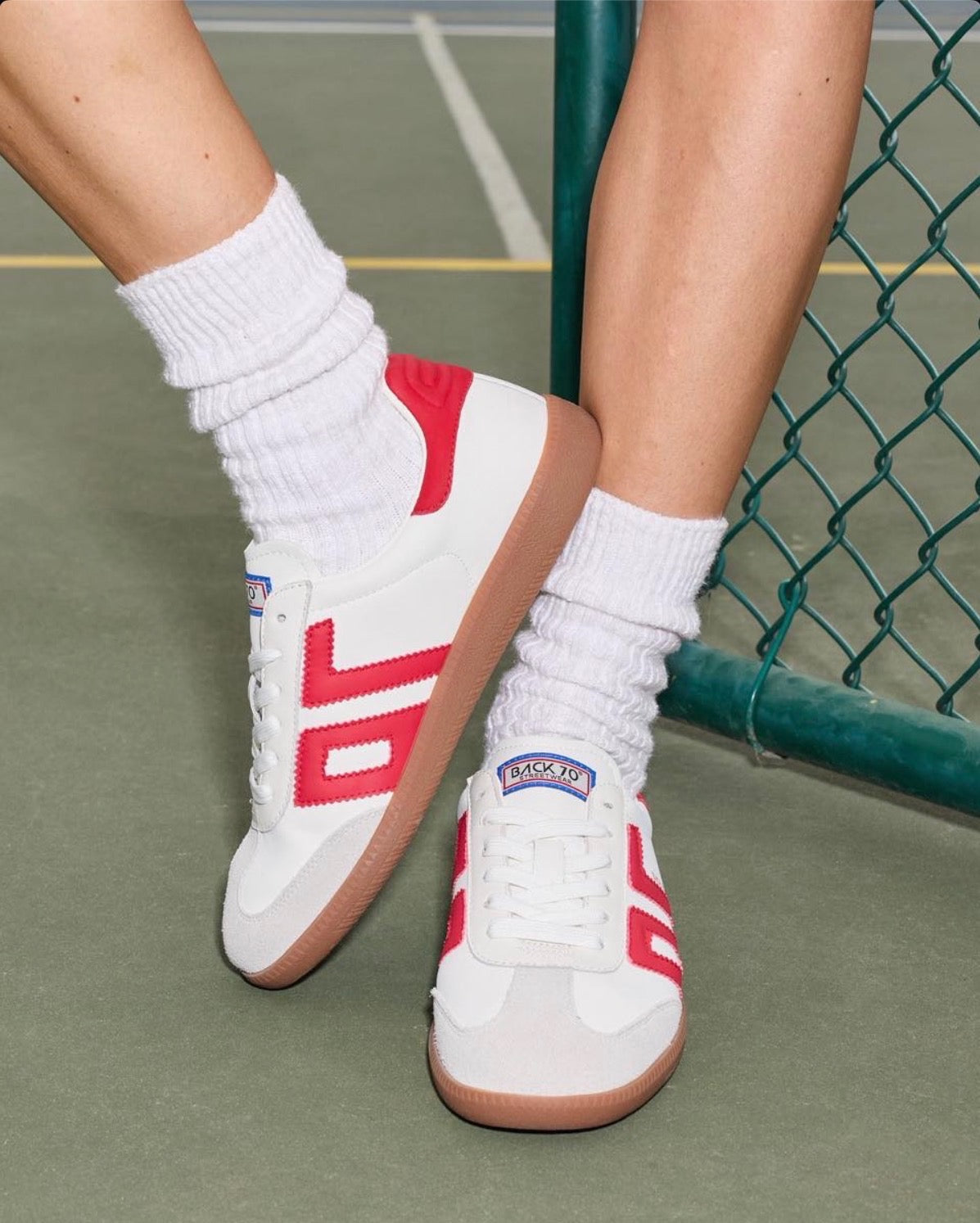 Close-up of feet wearing white and red retro sneakers with white crew socks on a tennis court